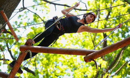 Mädchen klettert im Hochseilgarten über Stämme